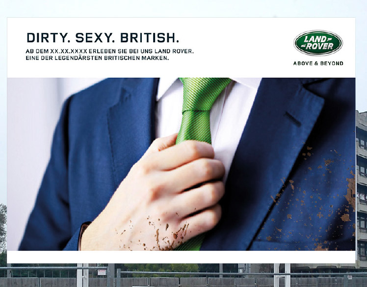 An image of a billboard outside of a construction site. 
                The billboard shows a close up of a person wearing a mud-splattered blue suit with a green tie and 
                the headline Dirty. Sexy. British.