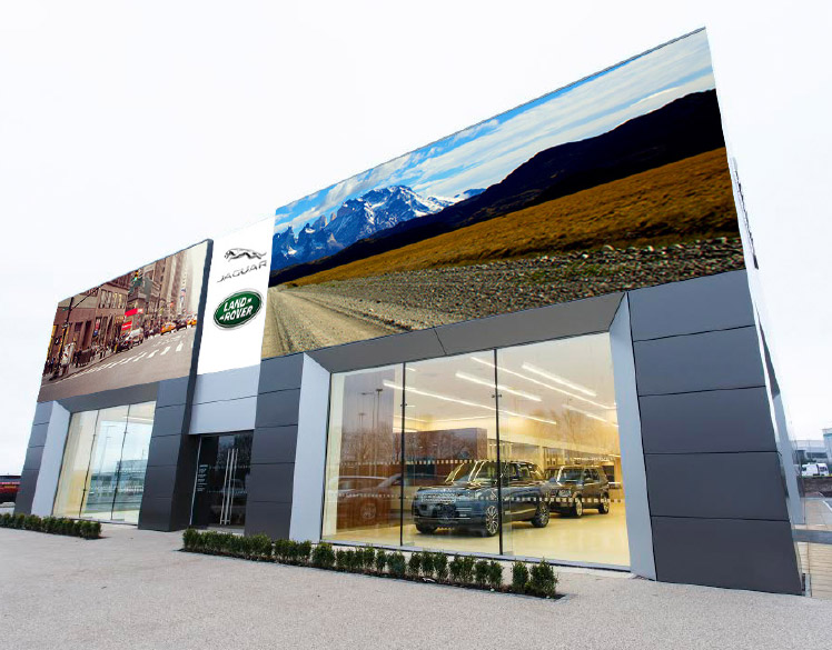 An image of a newly built car dealership. 
                A large sign above one window shows half a city street. A large sign above the other window shows 
                half a dirt road with mountains in the background. A headline in the middle, above the door of the building, 
                reads Egal Ob On Oder Off. Hauptsache Road.