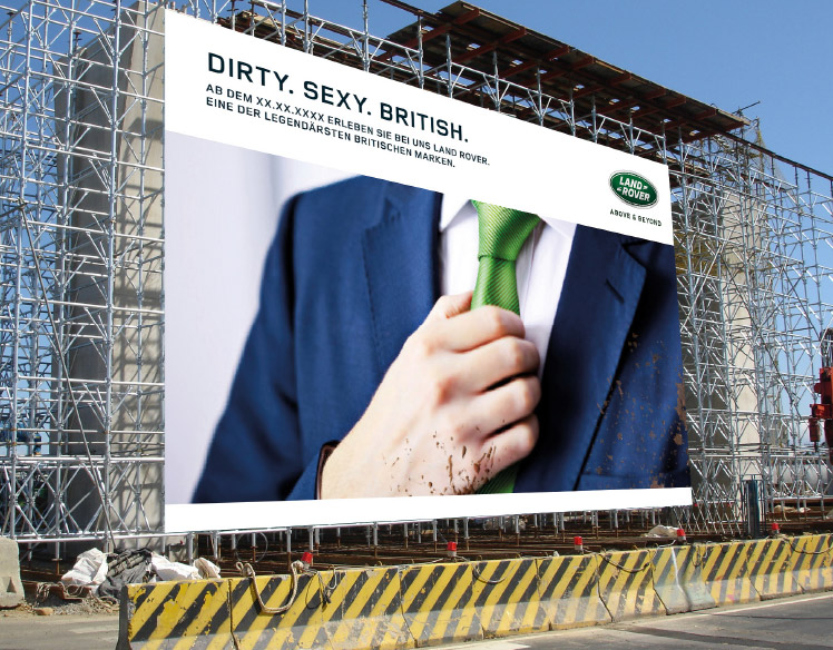 An image of scaffolding at a construction site. 
                The scaffolding is covered with a sign showing a close up of a person wearing a mud-splattered blue suit 
                with a green tie and the headline Dirty. Sexy. British.